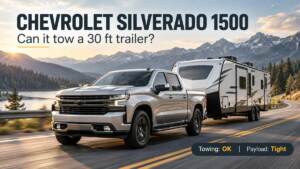 Silver Chevrolet Silverado 1500 crew cab towing a travel trailer on a mountain highway, with the question "Can it tow a 30 ft trailer?" and a badge reading Towing: OK, Payload: Tight